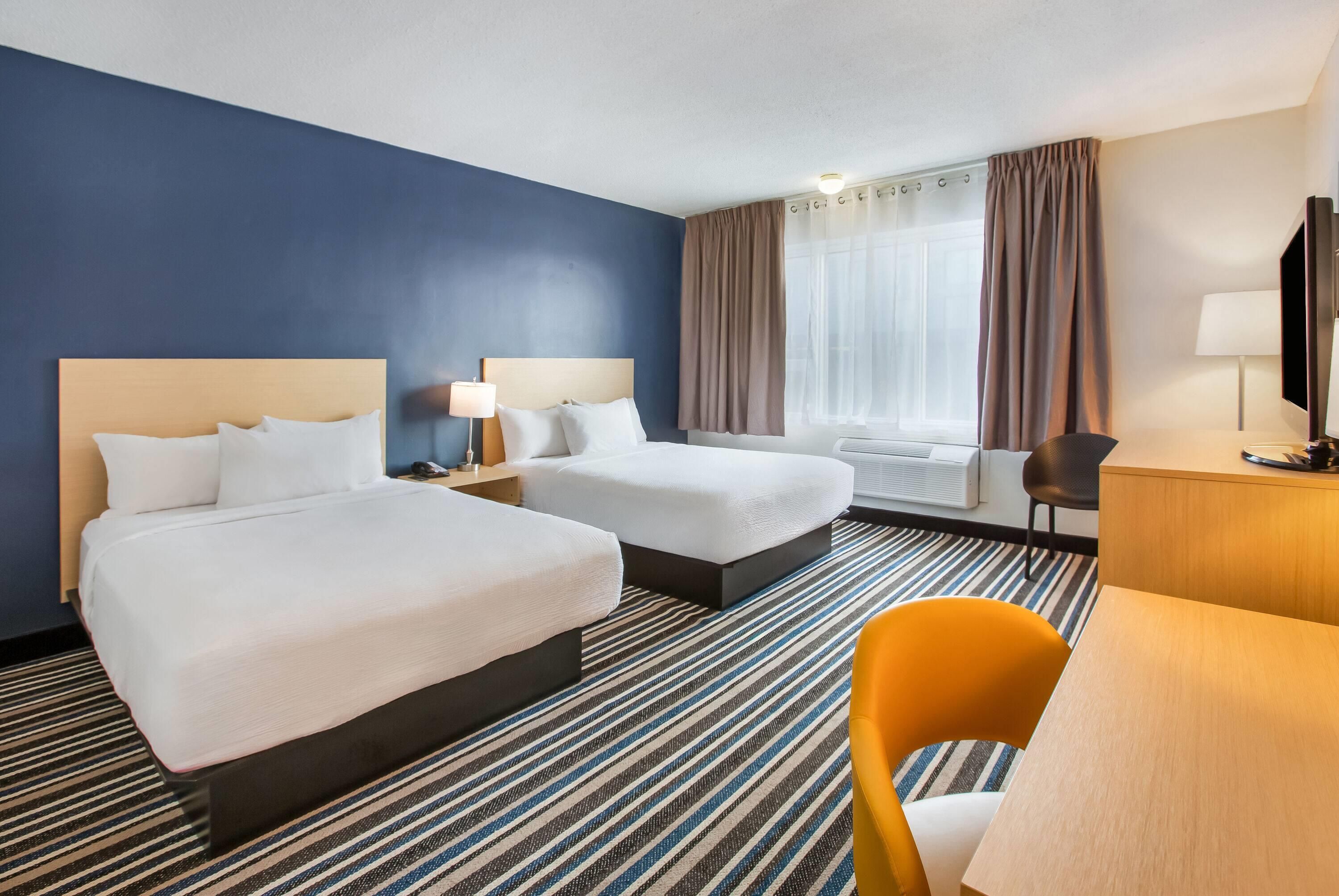 A hotel room with two beds, a desk, a chair, a TV, and a window with curtains.