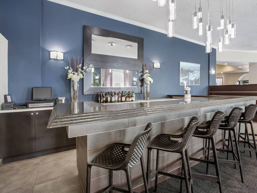 A modern bar area with a long counter, multiple bar stools, and a large mirror above the bar.