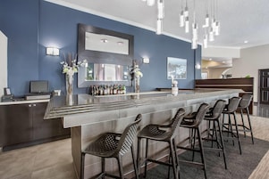A modern bar area with a long counter, multiple bar stools, and a large mirror above the bar.