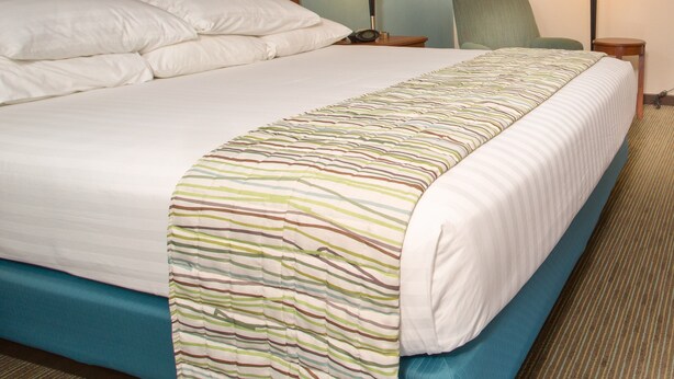 A hotel room with a large bed, two bedside lamps, a chair, and a wooden headboard. - Drury Inn & Suites Cape Girardeau (Cape Girardeau)