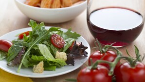 A plate of mixed greens salad with cherry tomatoes and croutons, a bowl of baked pasta, and a glass of red wine on a wooden table. - Drury Inn & Suites Cape Girardeau (Cape Girardeau)