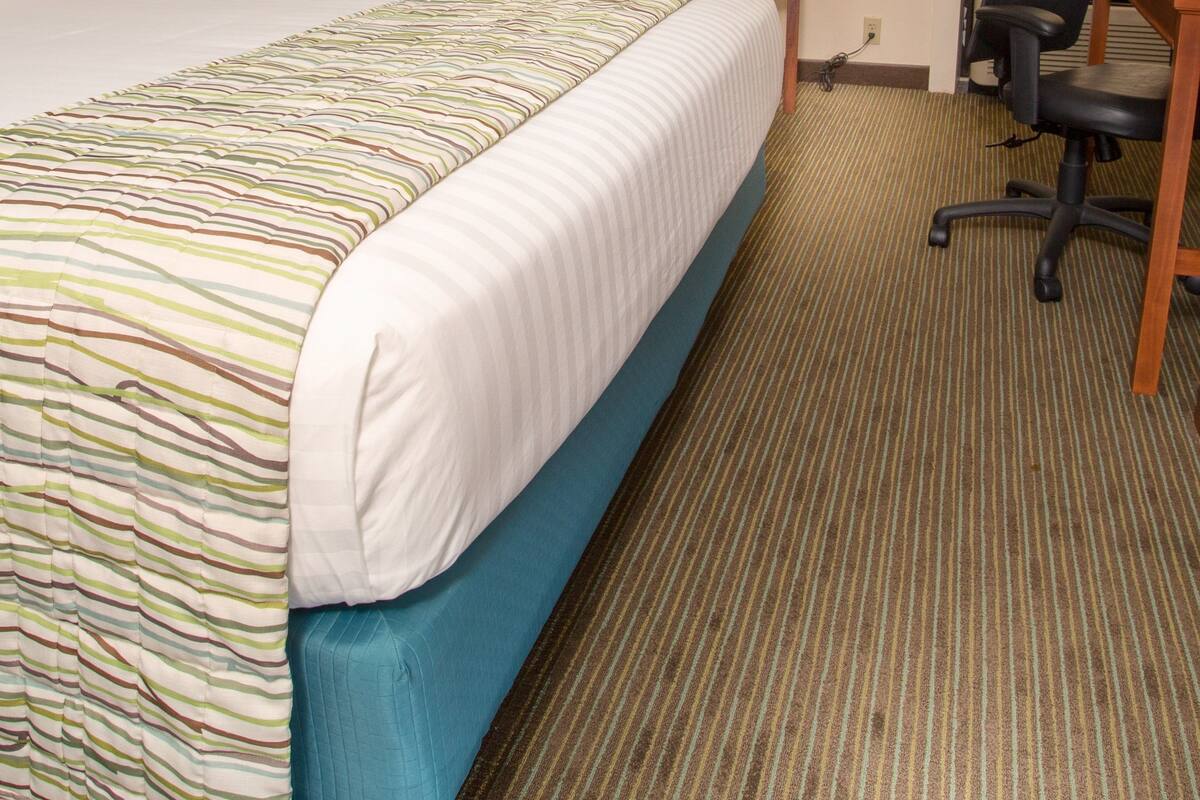 A hotel room with a large bed, two bedside tables, a desk with a chair, and two lamps.