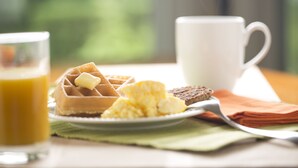 A breakfast setting with waffles, scrambled eggs, toast, a glass of orange juice, and a white mug on a table with a green placemat. - Drury Inn & Suites Cape Girardeau (Cape Girardeau)