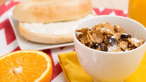 A bowl of cereal with raisins and milk, a half orange, and a sandwich on a table with a yellow napkin. - Drury Inn & Suites Cape Girardeau (Cape Girardeau)