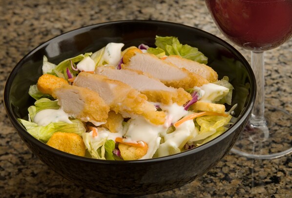 A bowl of salad with breaded chicken and croutons, accompanied by a glass of red wine.