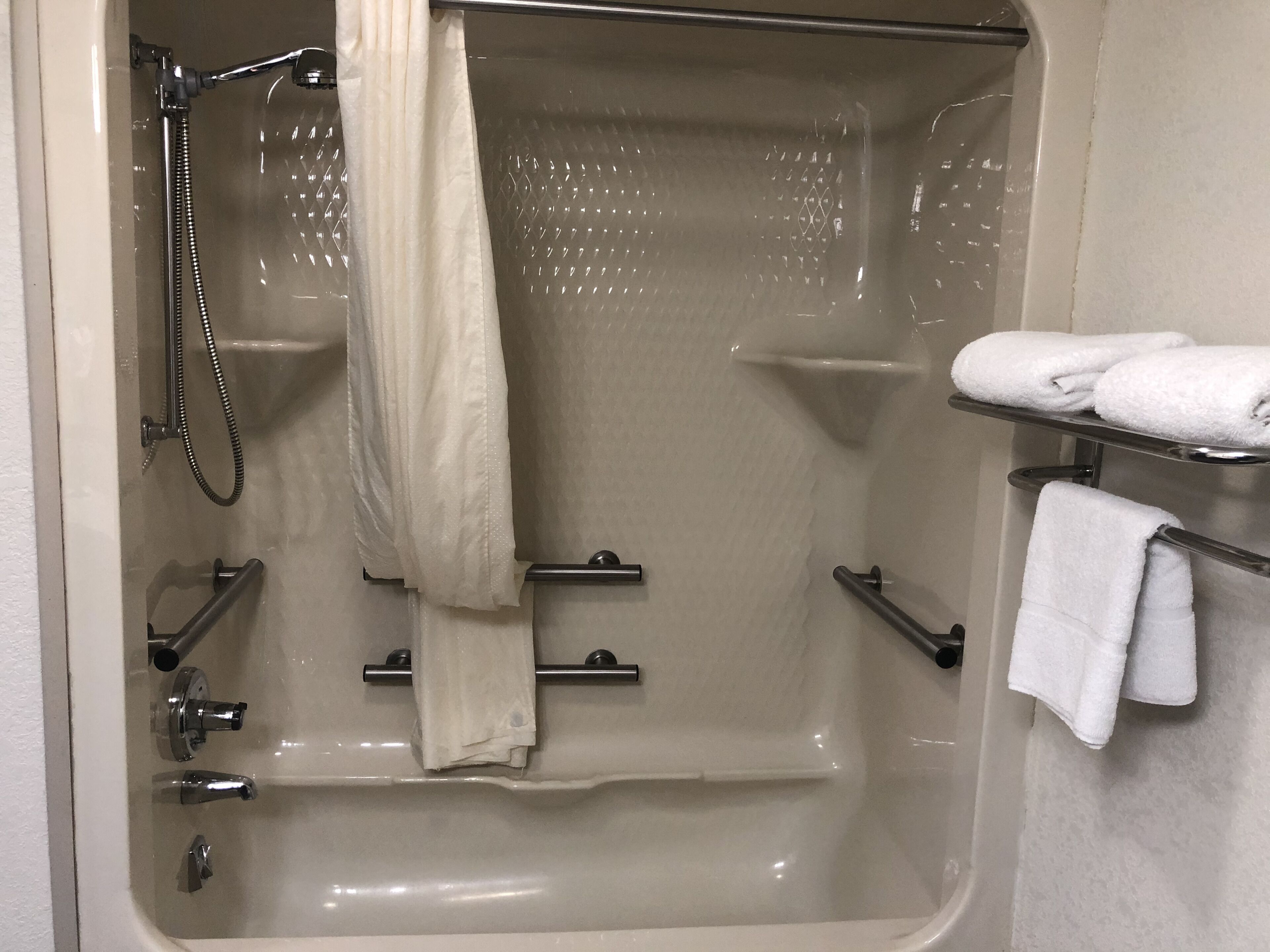 A bathtub with a shower head, a towel rack, and a shelf with towels.