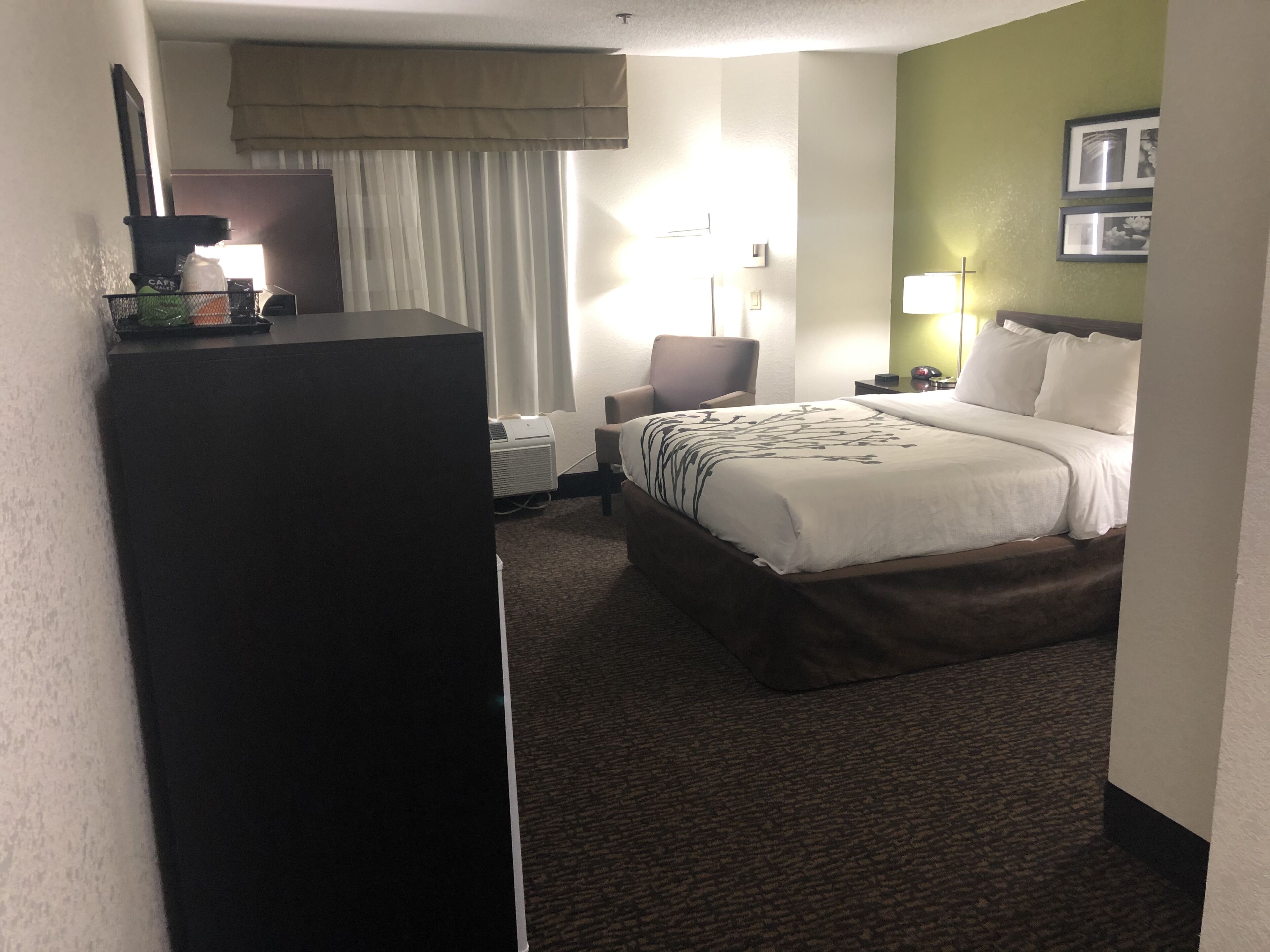 A hotel room with a bed, a chair, a desk, and a lamp.