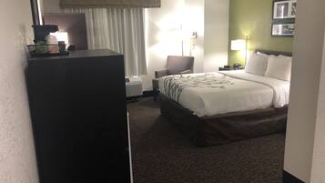 A hotel room with a bed, a chair, a desk, and a lamp.