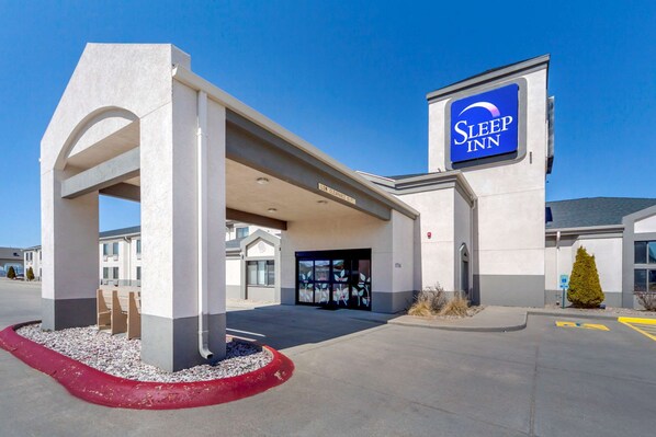 A Sleep Inn hotel entrance with a clear sky, a parking lot, and a red curb.