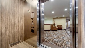 An elevator with a control panel and a patterned carpeted floor.
