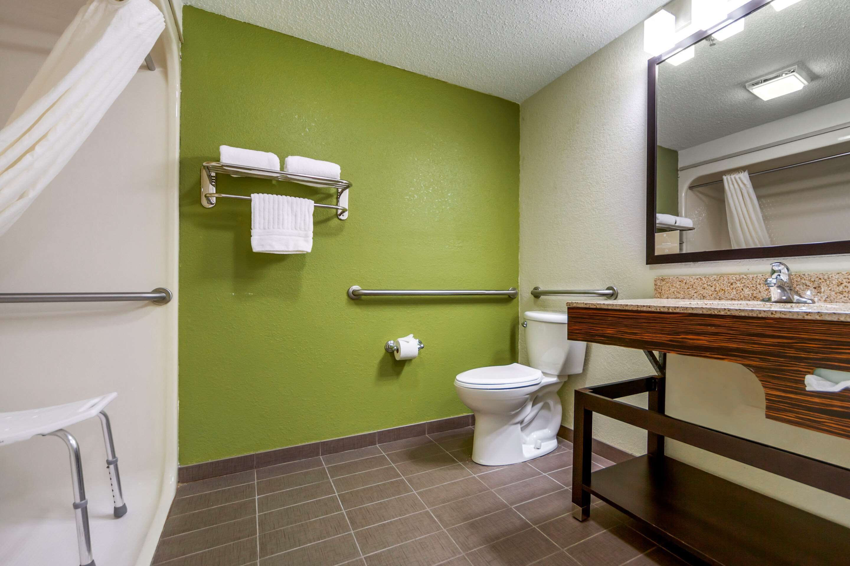 A bathroom with a green wall, a white toilet, a sink with a mirror, and a towel rack.
