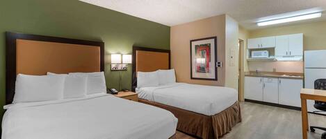 A hotel room with two beds, a small kitchenette, and a desk.