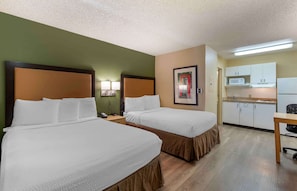 Ein Hotelzimmer mit zwei Betten, einer kleinen Küchenzeile und einem Schreibtisch.