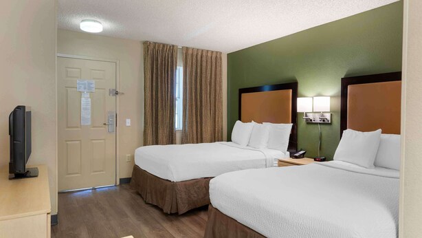 A hotel room with two beds, a TV, a desk, and a window with curtains.