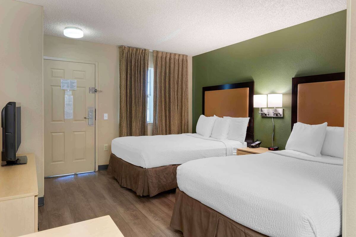 Habitación de hotel con dos camas, televisión, escritorio y ventana con cortinas.