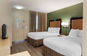 Ein Hotelzimmer mit zwei Betten, einem Fernseher, einem Schreibtisch und einem Fenster mit Vorhängen.