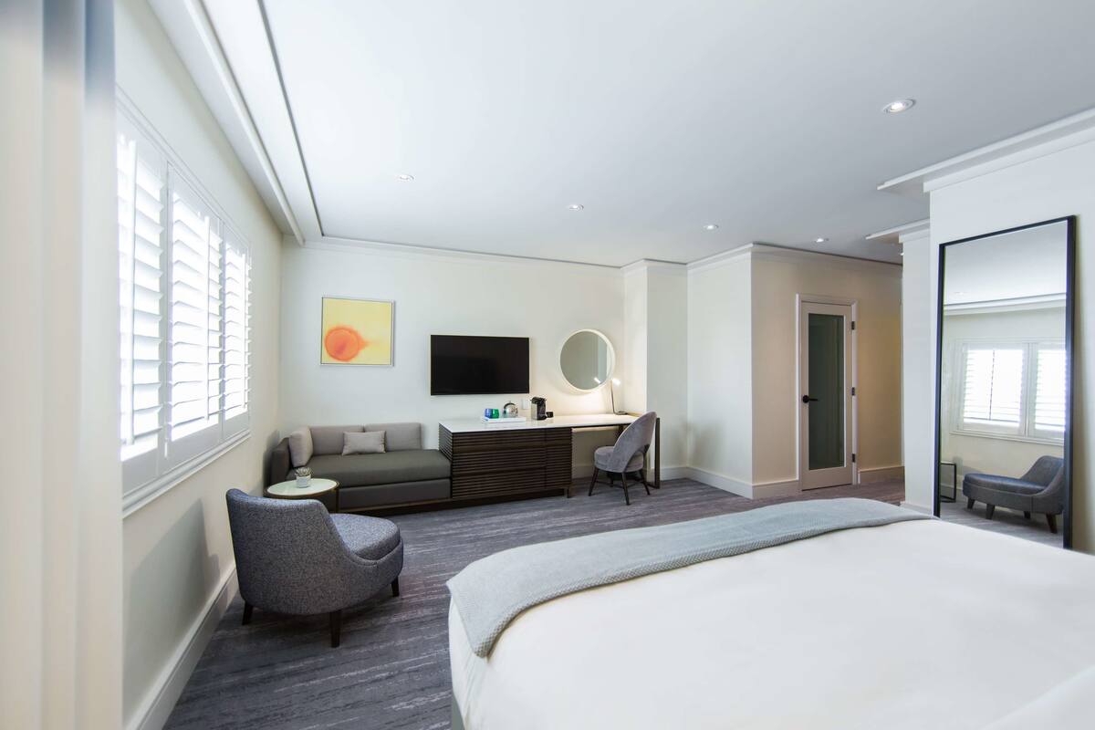 A modern hotel room with a bed, a desk, a chair, a sofa, and a TV.