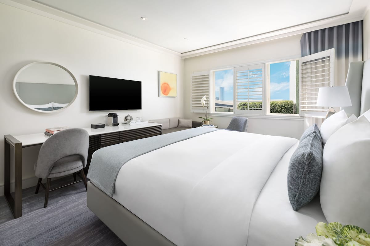 A modern hotel room with a large bed, a desk, a chair, a television, and a window with blinds.