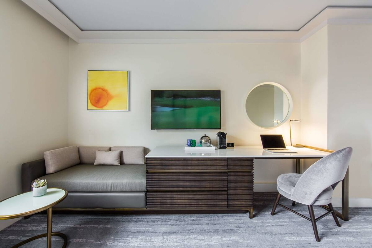 A modern room with a sofa, a desk, a chair, a round mirror, and two artworks on the wall.