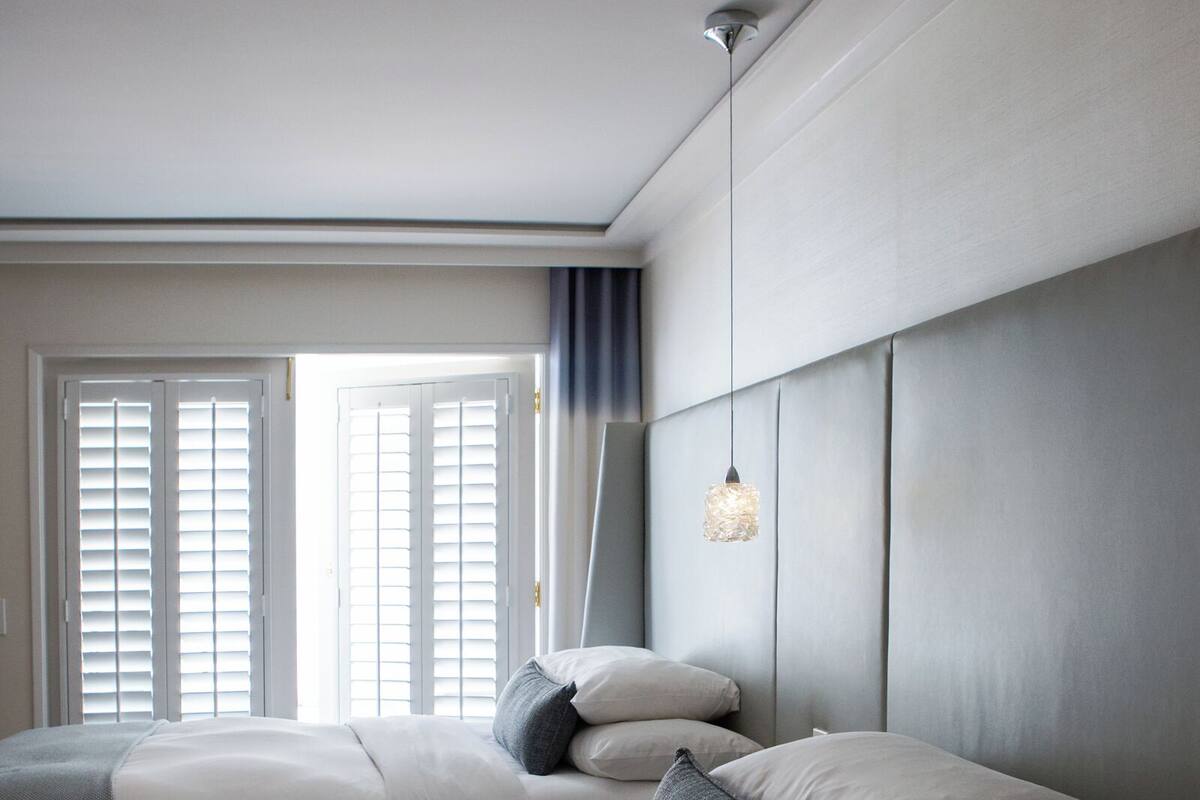 A hotel room with a large bed, a smaller bed, a hanging light fixture, and a view of the outside through the window.
