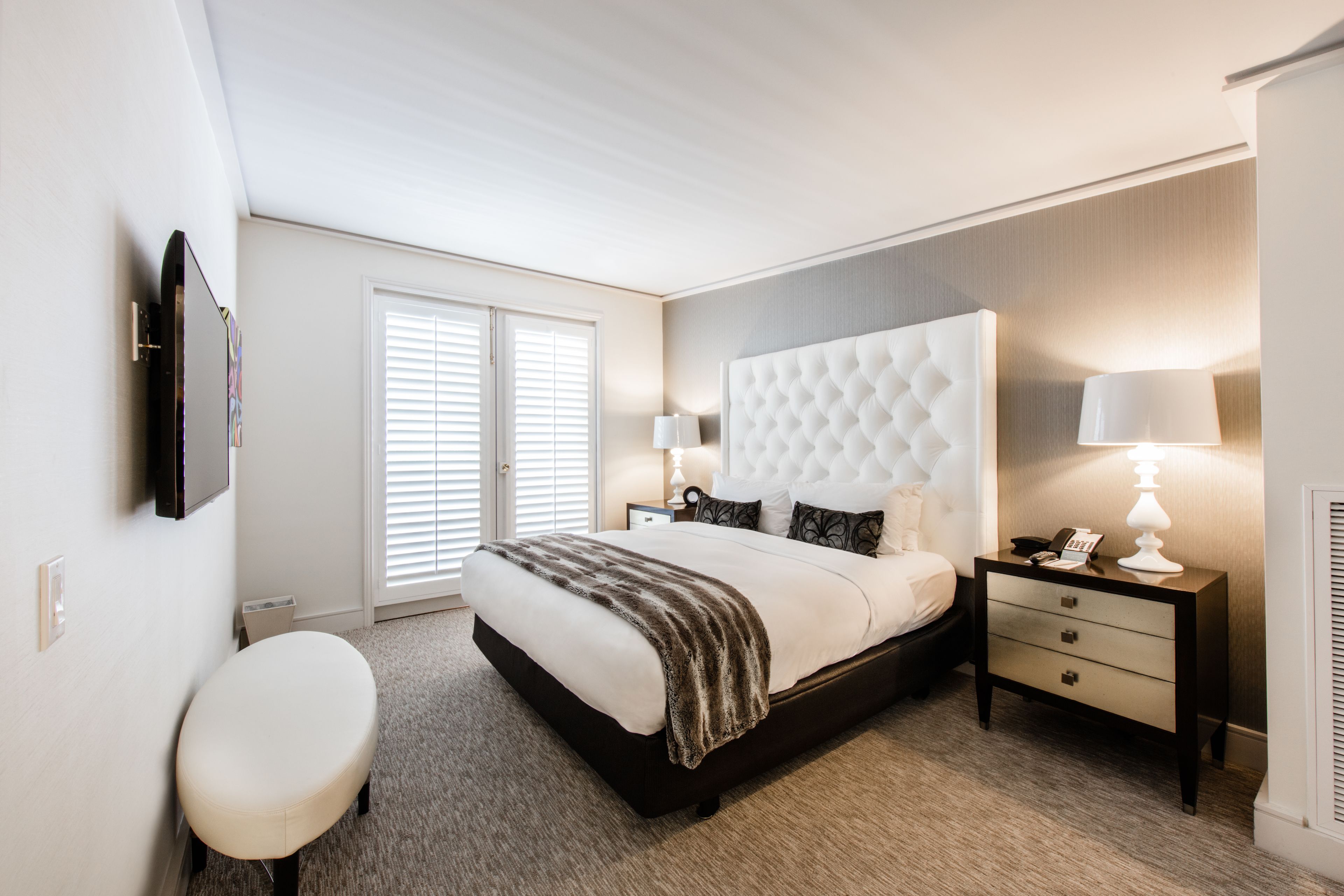 Une chambre à coucher moderne avec un grand lit, des tables de chevet, un banc et un téléviseur fixé au mur.