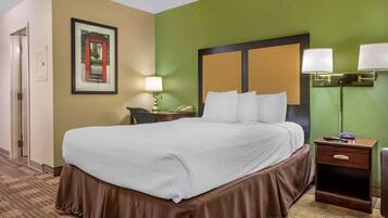 Una habitación de hotel con una cama grande, una mesita de noche con una lámpara, un cuadro en la pared y una pared decorada en color verde.