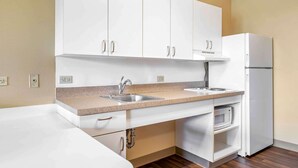 A compact kitchen with white cabinets, a double sink, a microwave, and a refrigerator.