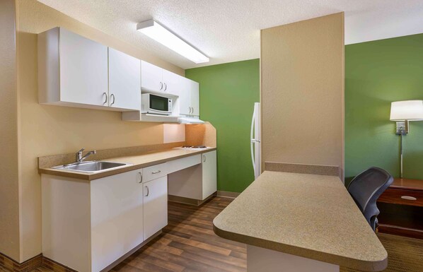 A compact kitchen with white cabinets, a microwave, a refrigerator, and a sink.
