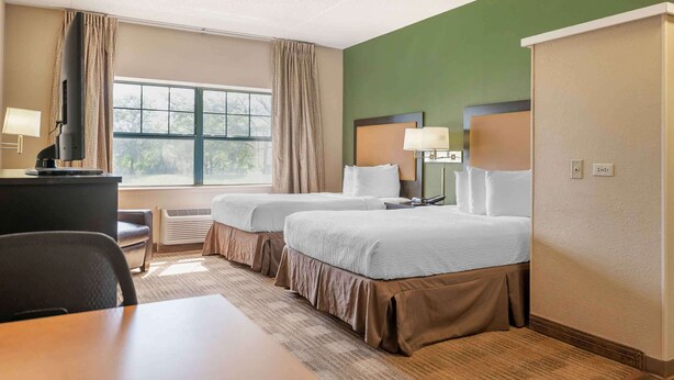 A hotel room with two beds, a desk, a chair, a TV, and a window with curtains.
