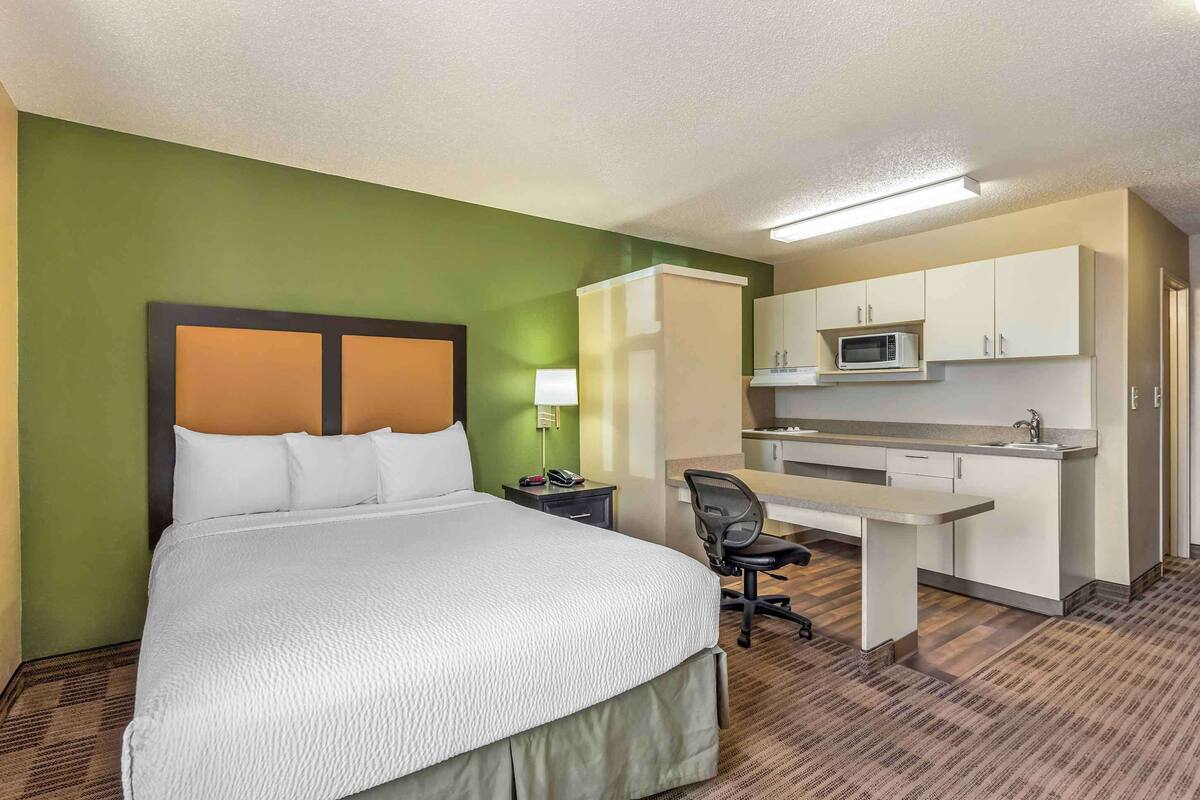 A hotel room with a bed, desk, kitchenette, and a green wall.