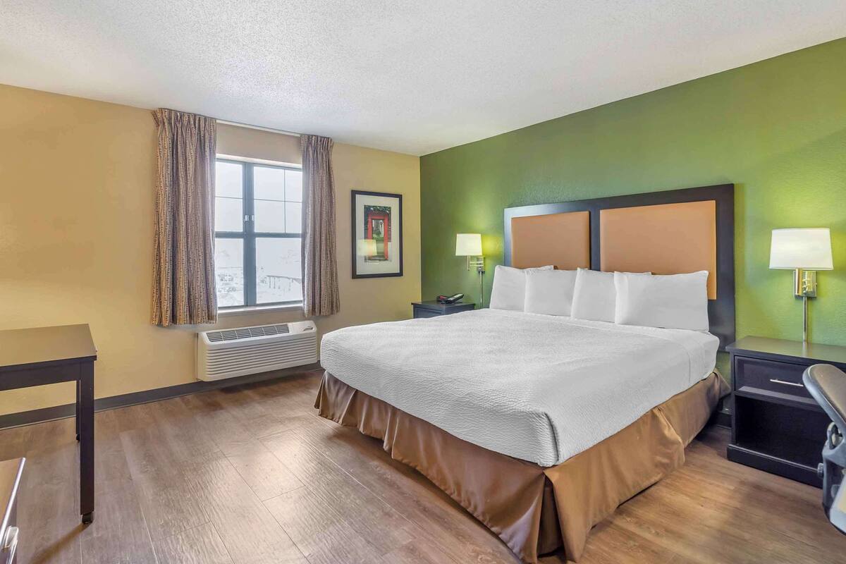 A hotel room with a large bed, two bedside tables with lamps, a window with curtains, and a picture on the wall.