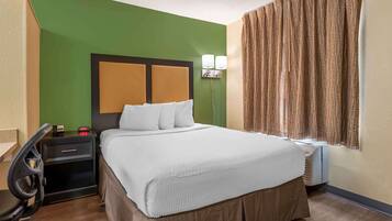 A hotel room with a bed, a nightstand, a chair, and a window with curtains.