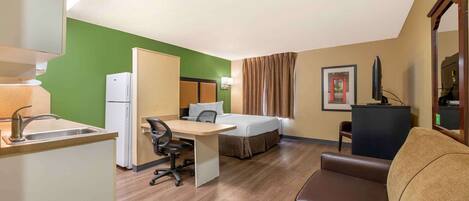 Una habitación de hotel compacta con kitchenette, una cama, un escritorio y un sofá.