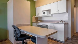 A compact kitchen with white cabinets, a microwave, and a small dining area with a chair.