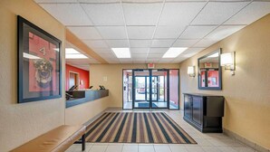 A hotel lobby with a reception desk, a bench, a striped carpet, and a glass door leading outside.