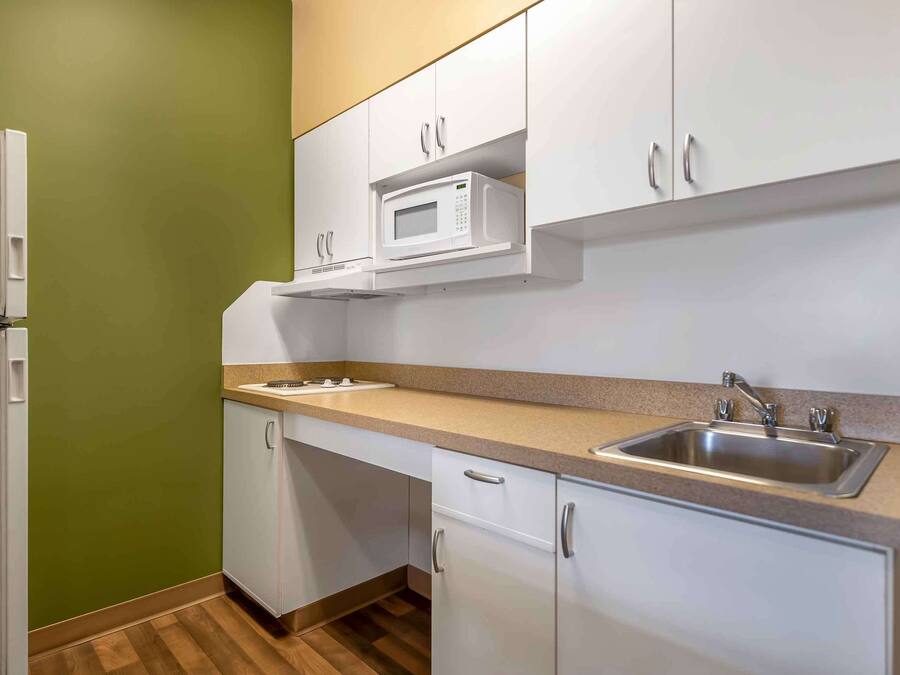 Una cocina compacta con armarios blancos, microondas, pileta y piso de madera.
