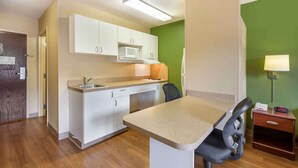 Une cuisine compacte avec des meubles blancs, un four à micro-ondes, un évier et une petite table à manger avec une chaise.