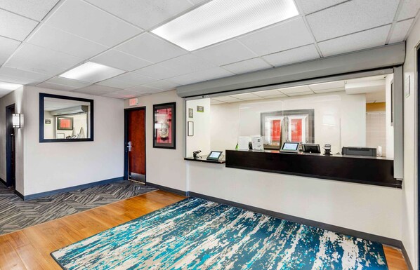 A reception area with a reception desk, a large mirror, a wooden floor, and a blue and white patterned rug.