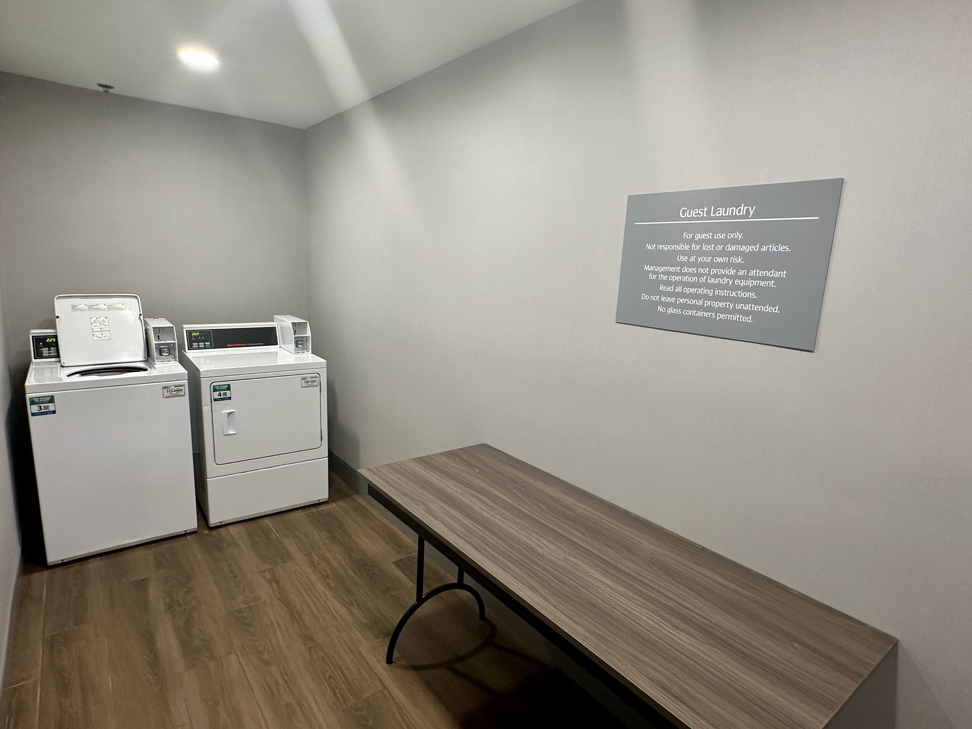 A laundry area with two washing machines and a table. A sign on the wall provides laundry instructions.