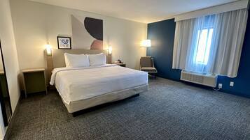 A hotel room with a large bed, two bedside tables, a chair, a wall-mounted lamp, and a window with curtains.