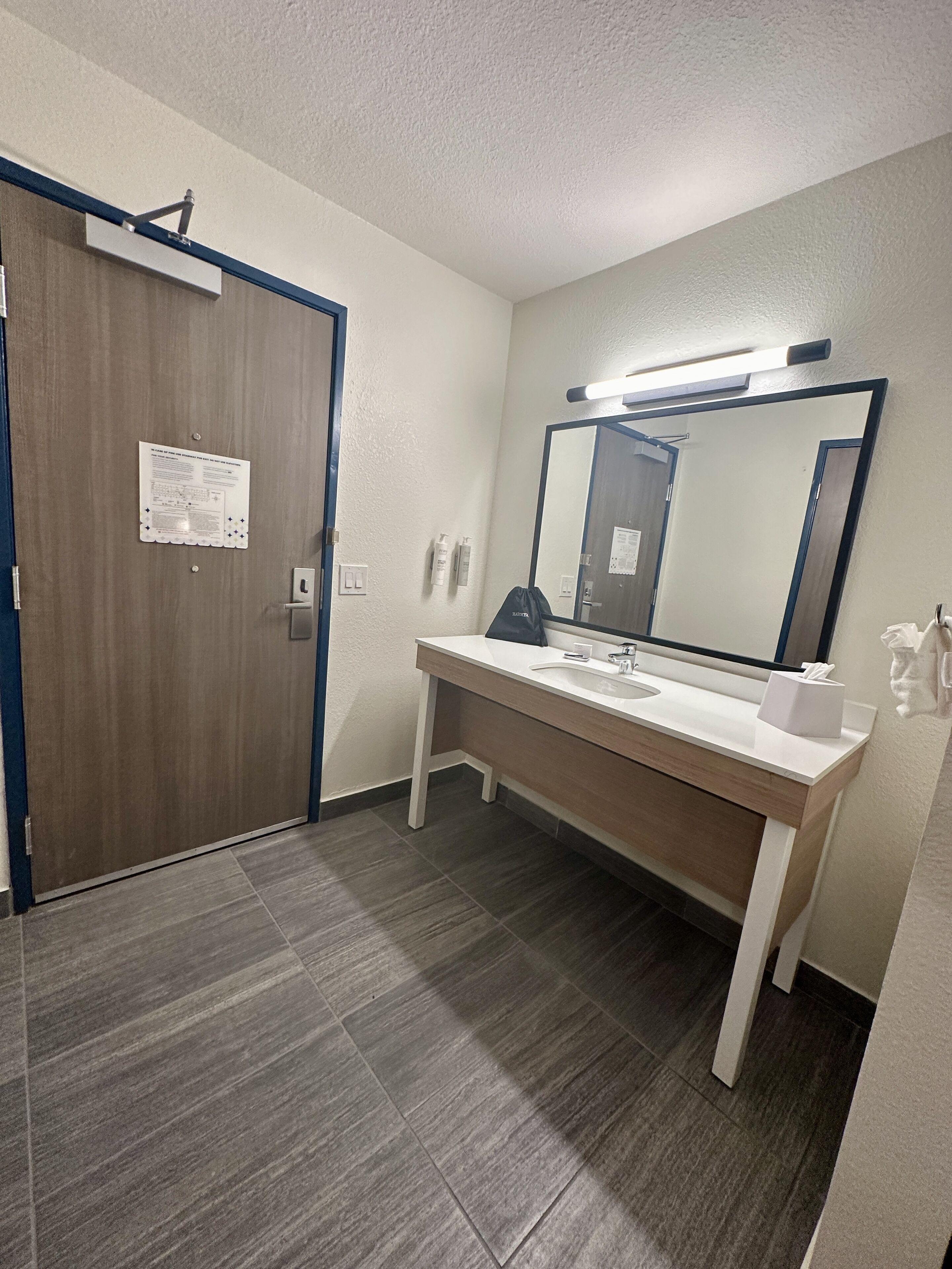 Une salle de bain d’hôtel avec une porte en bois, un lavabo avec un miroir et un porte-serviettes.