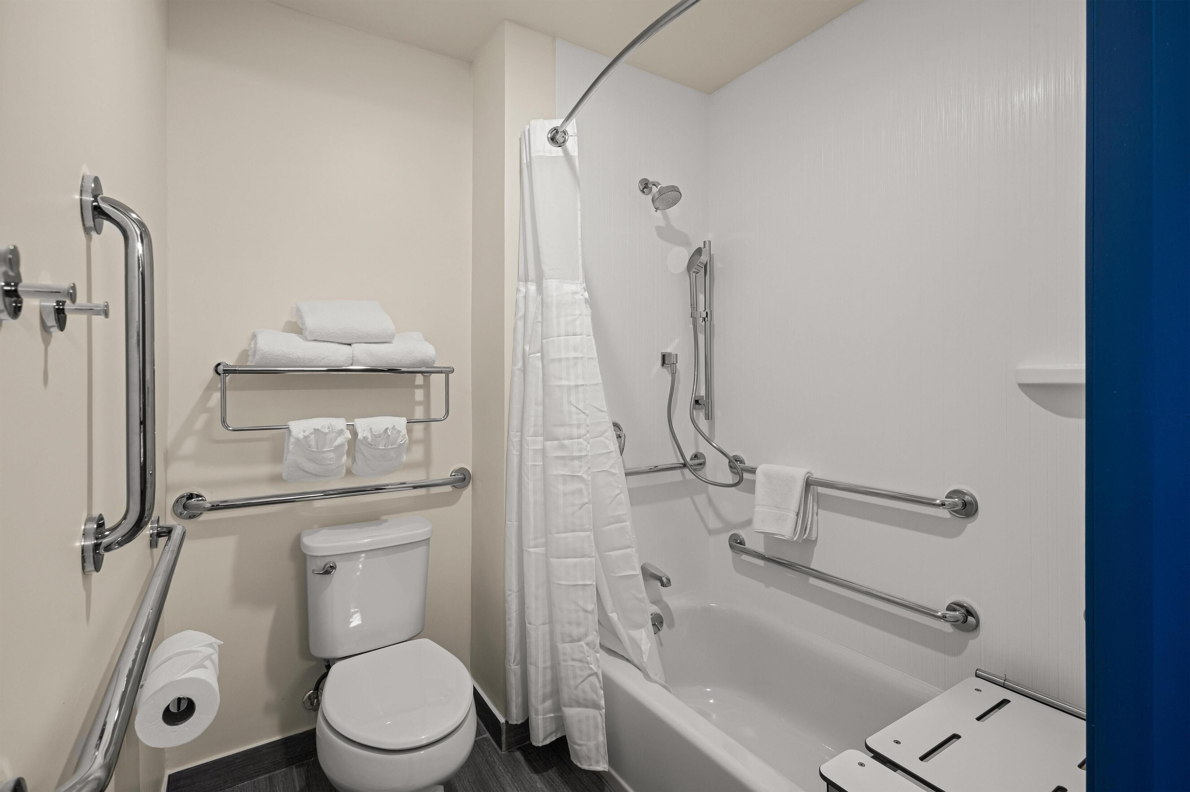 A modern bathroom with a toilet, shower, and grab bars.