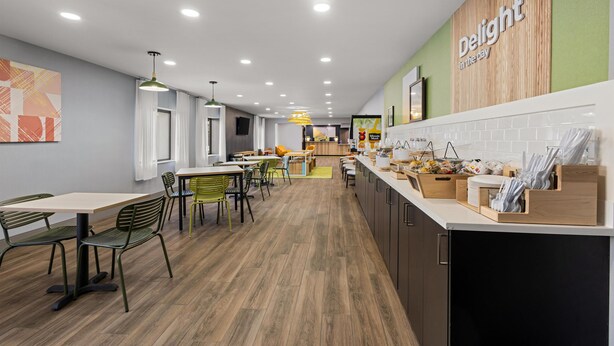 Een modern restaurant met een houten accentmuur, groene stoelen en een toonbank met diverse artikelen.