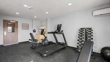 Un gimnasio con cintas de correr, una banca y equipo de levantamiento de pesas.