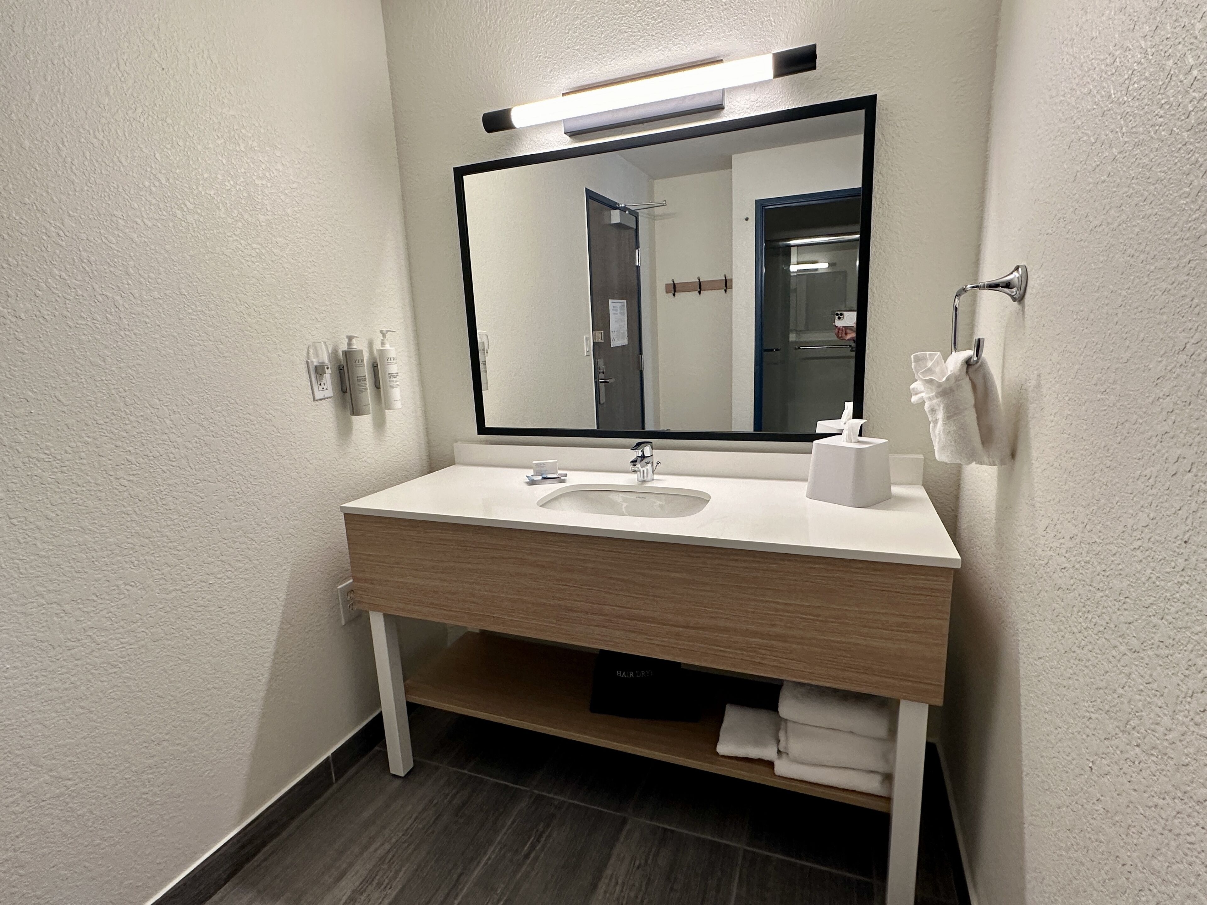 Un baño moderno con tocador blanco, un espejo grande y un perchero para toallas.