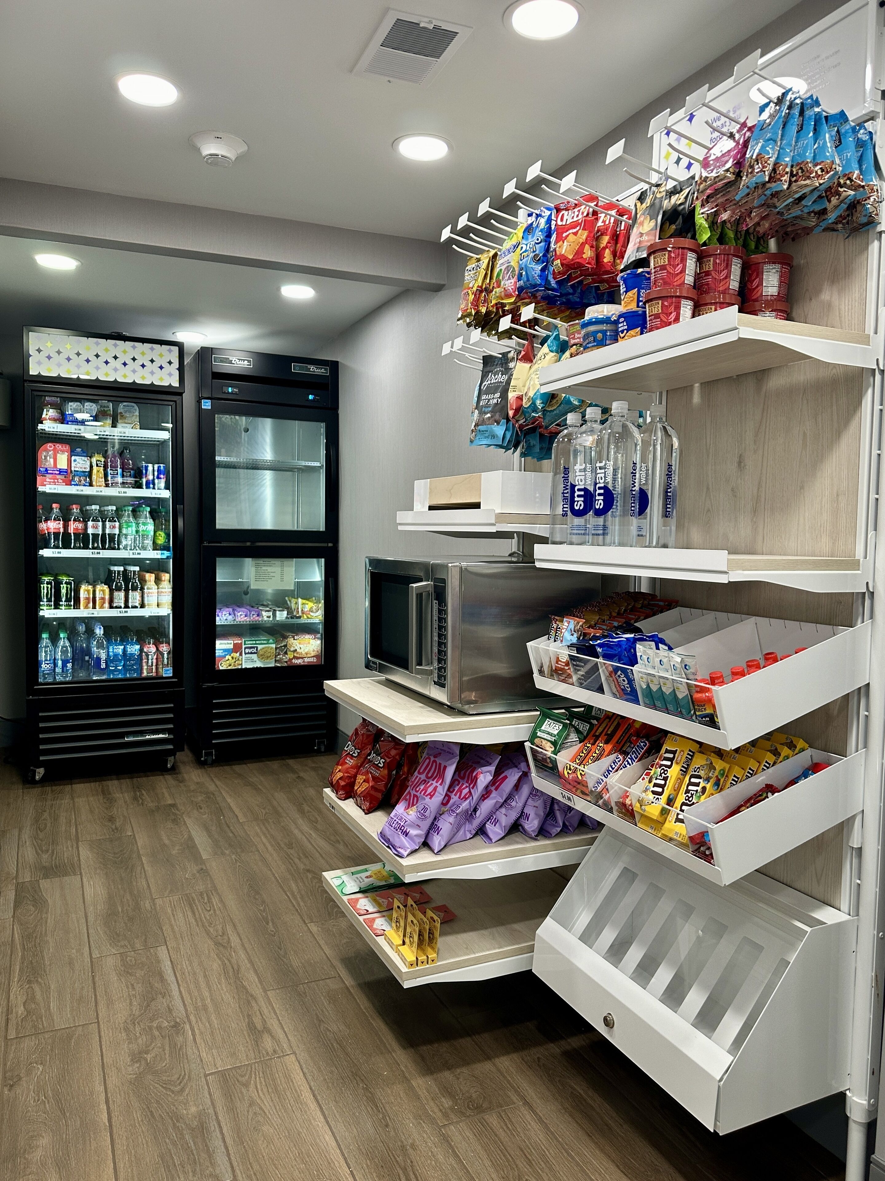 A store with shelves stocked with snacks and bottled water, and two refrigerators with beverages.