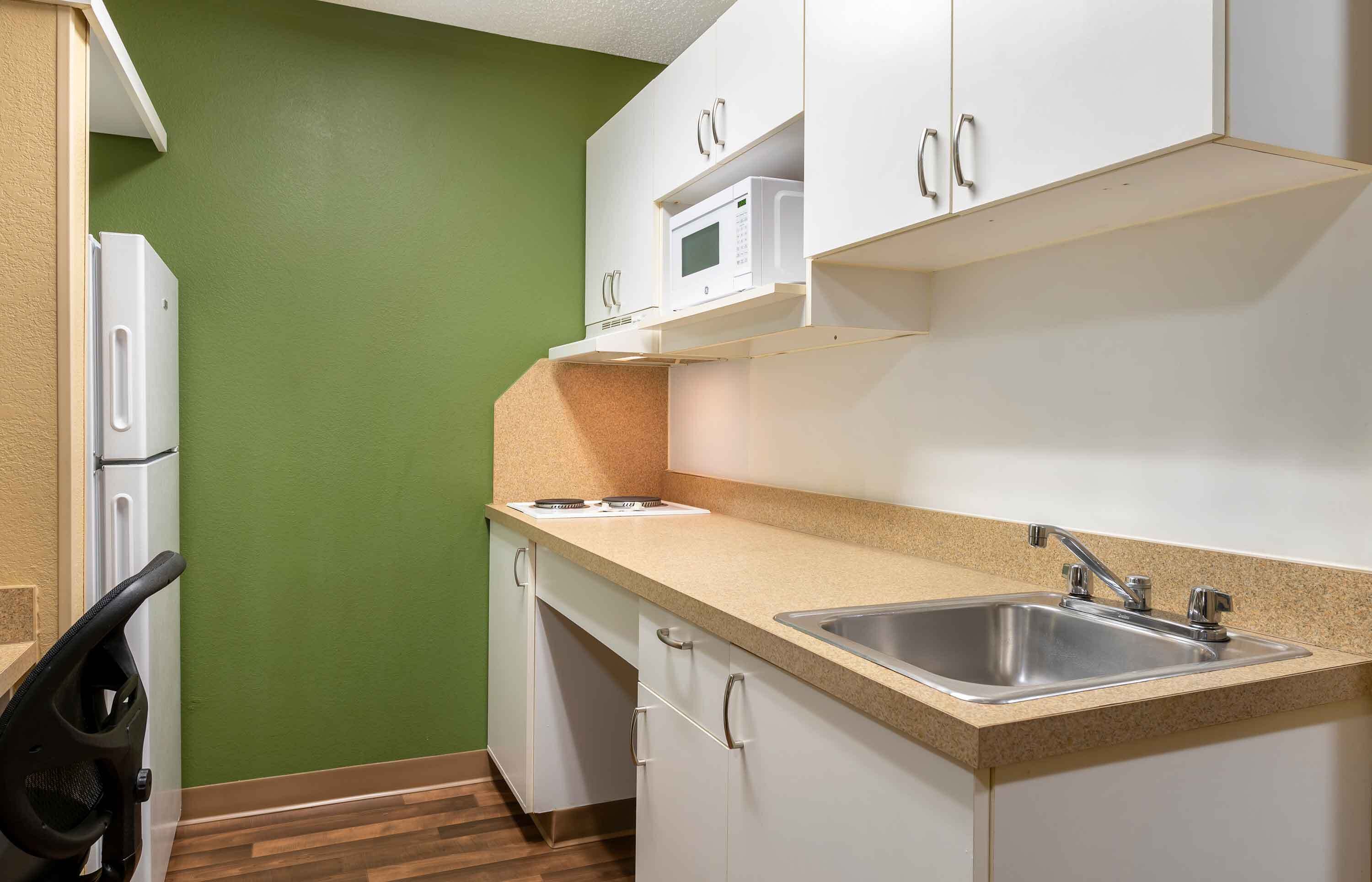 Una cocina compacta con gabinetes blancos, un microondas y un lavamanos.