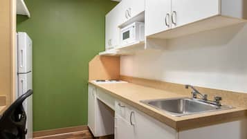 Una cocina compacta con gabinetes blancos, un microondas y un lavamanos.