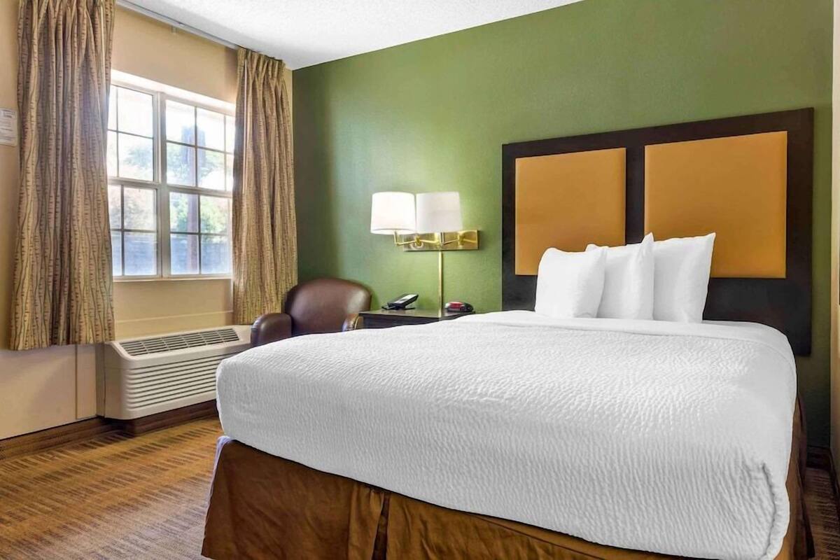 Una camera d'albergo con un letto grande, una scrivania con una lampada, una sedia e una finestra con tende.