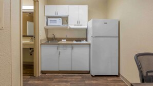 Una cocina compacta con armarios blancos, un microondas y un refrigerador.